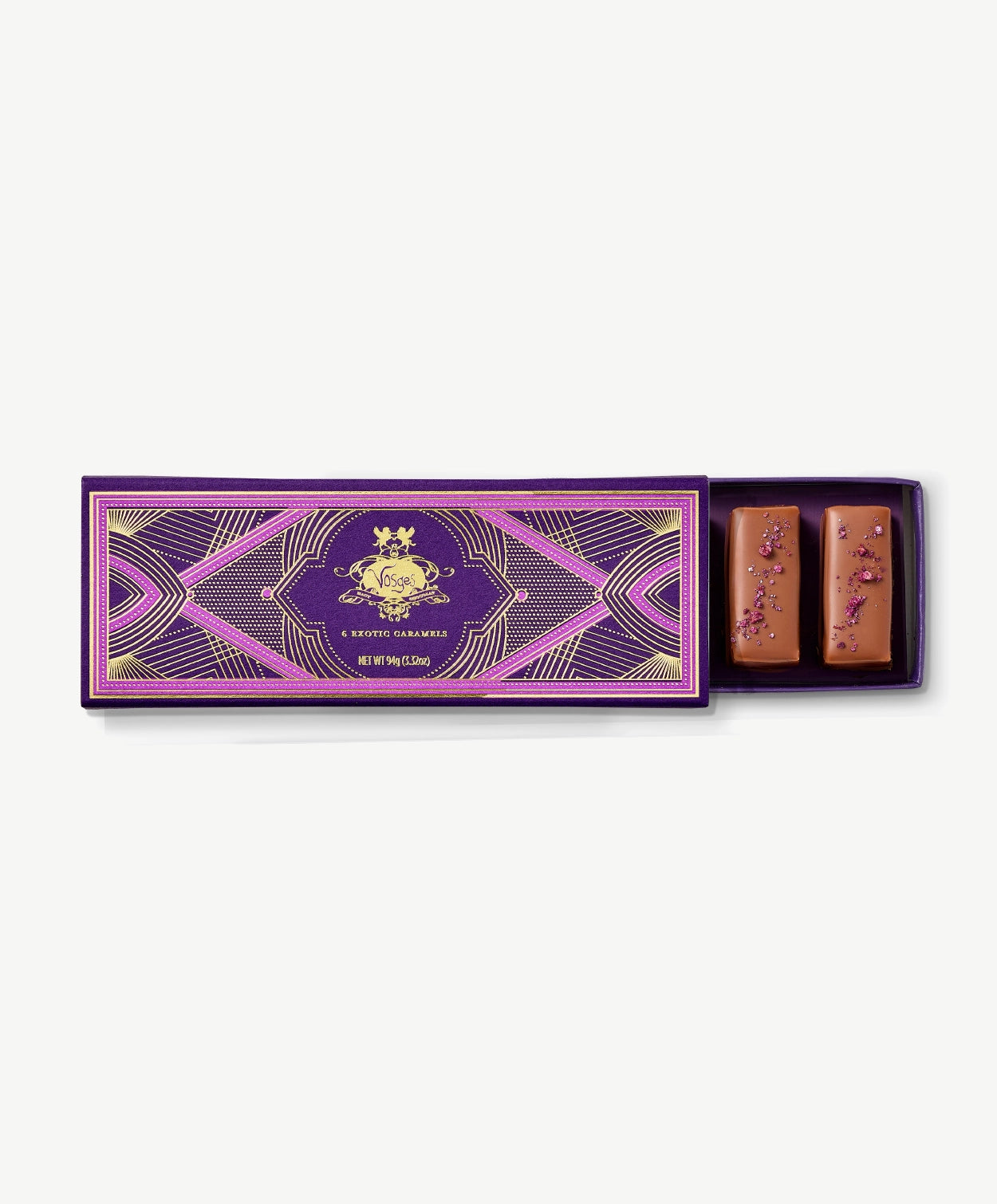 Purple Vosges chocolate box opened revealing two chocolate covered caramels adorned with chopped pecans on a grey background.