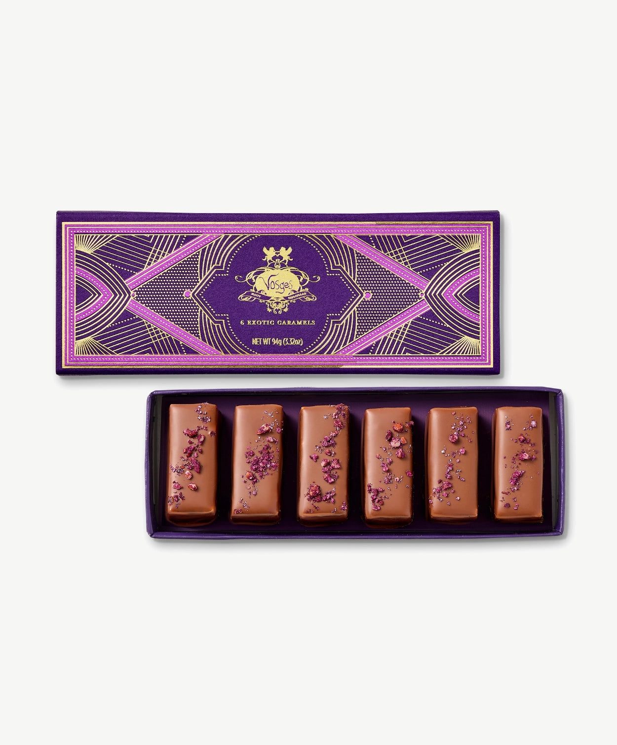 Six chocolate covered Vosges Caramels topped with crushed pecans in opened candy box embossed with gold foil on a grey background.